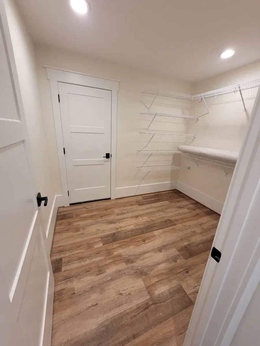 Empty walk-in closet with wire shelves, a closed white door, and wood-look flooring.