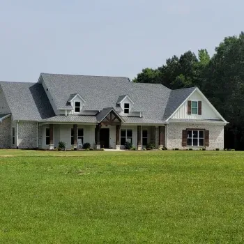Large, light-colored brick house with gray roof, dormers, and a wide green lawn.