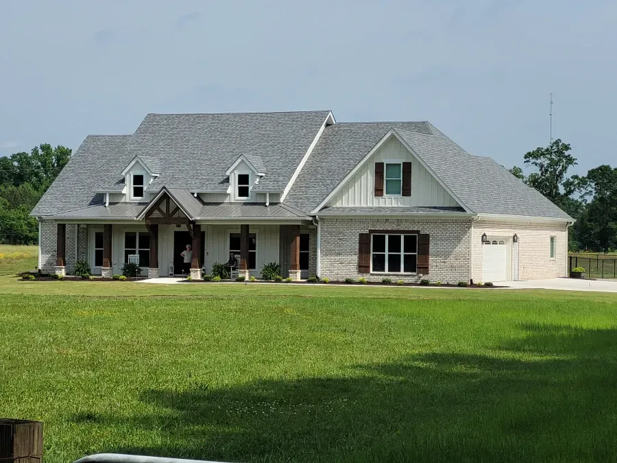 A light-colored house with gray roof, brown shutters, and a green lawn under a blue sky.