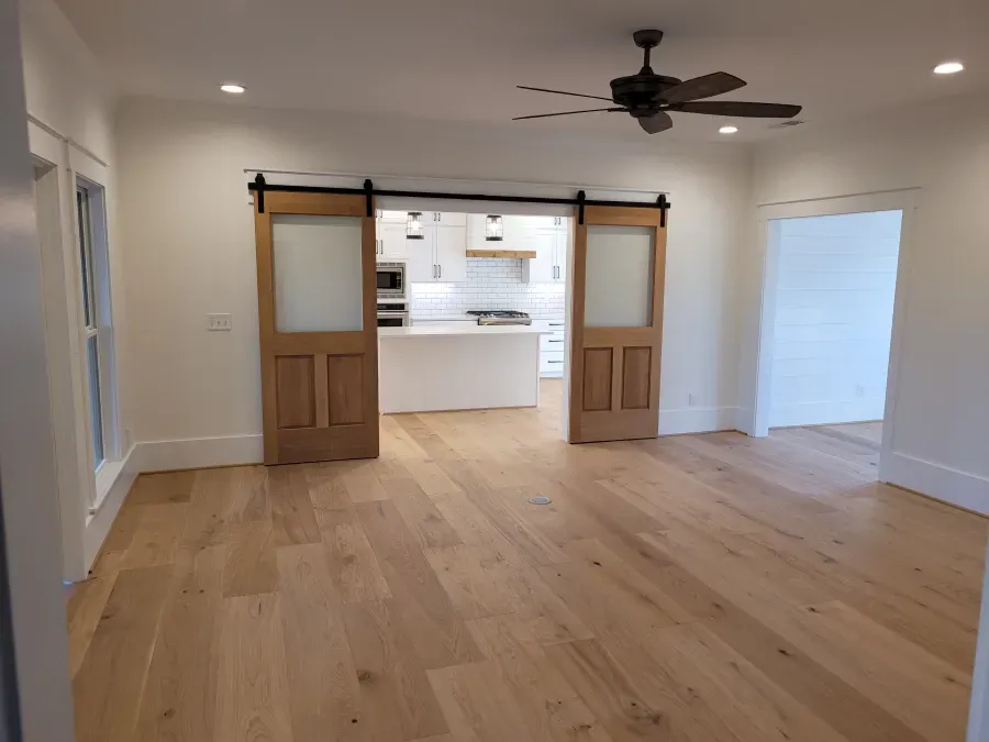 Wooden barn doors open to a kitchen. Light wood floors and white walls.