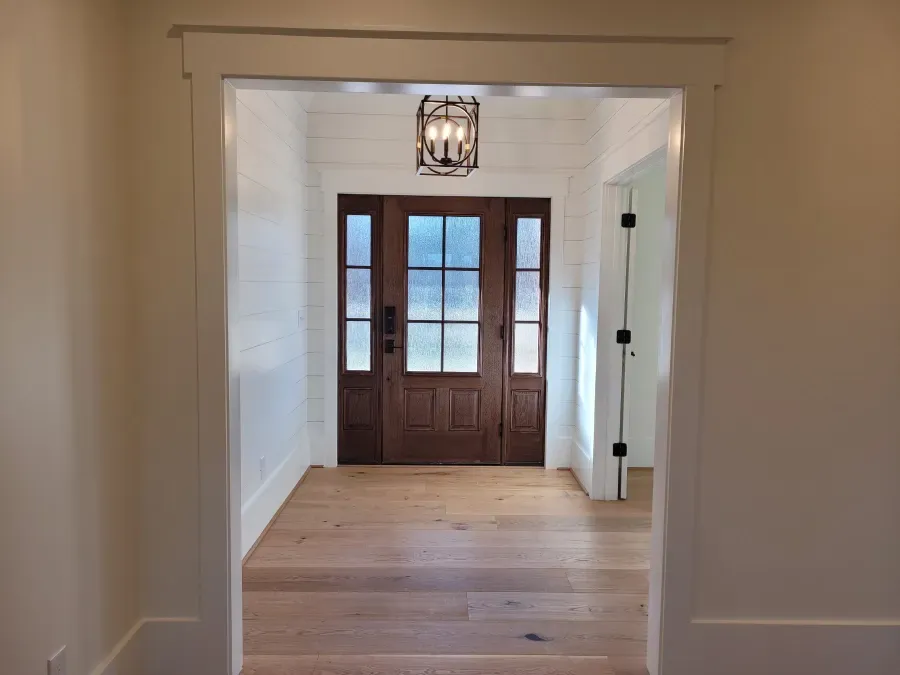 Entryway with wooden door, wood floors, white walls and trim.