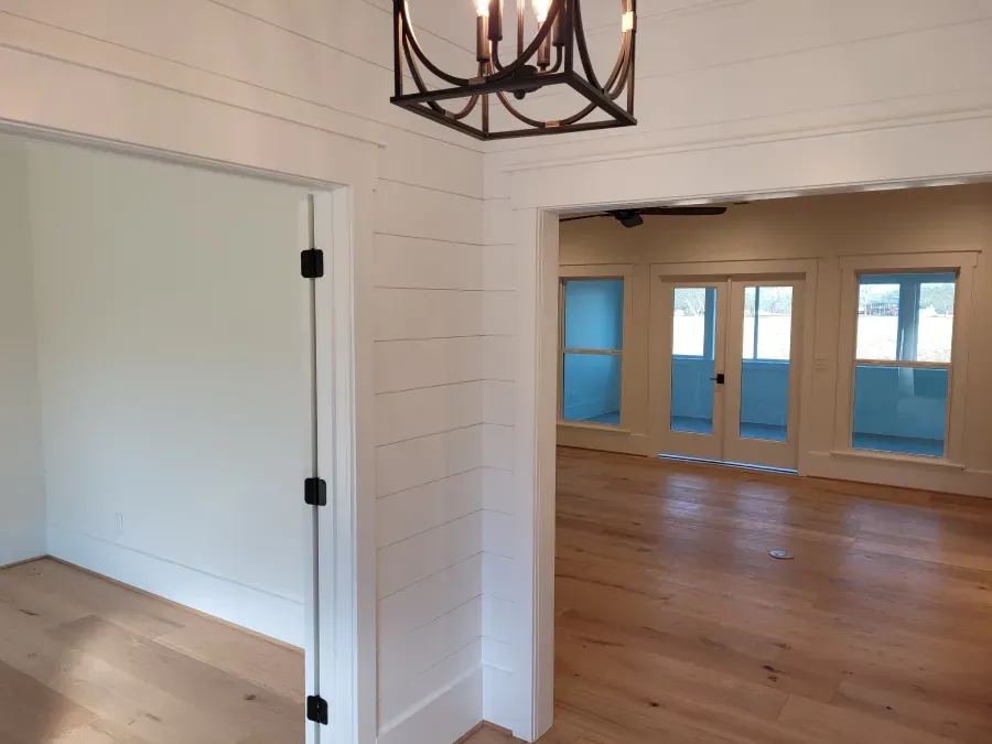 Interior view of a room with white plank walls, hardwood floors, and a doorway to a room with glass doors.
