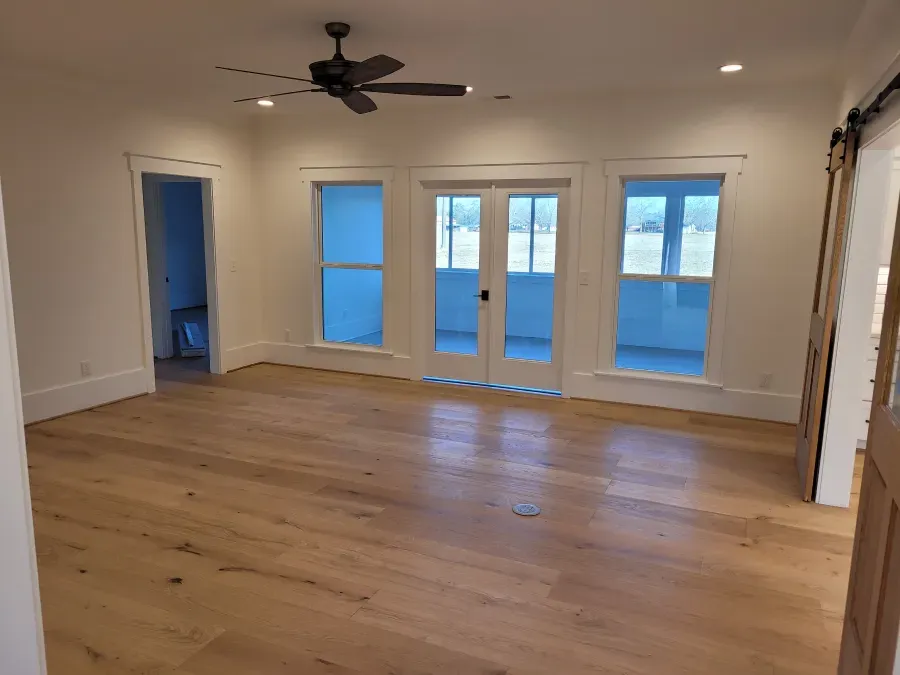 Empty room with hardwood floors, white walls, French doors, windows, and a ceiling fan.