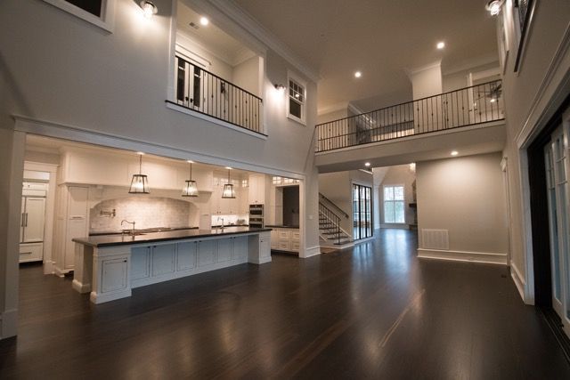 Spacious, modern interior with kitchen, dark wood floors, balcony, and staircase. Neutral colors, well-lit.