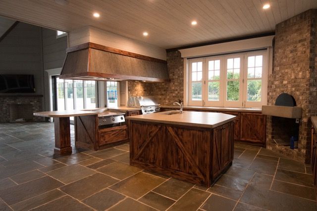 Rustic kitchen with stone floor, wood cabinets, large range hood, island, and brick accents.