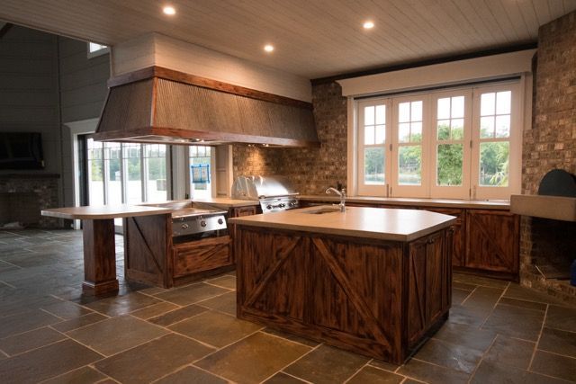 Rustic kitchen with stone walls, wooden island, stainless steel range hood, and large windows.