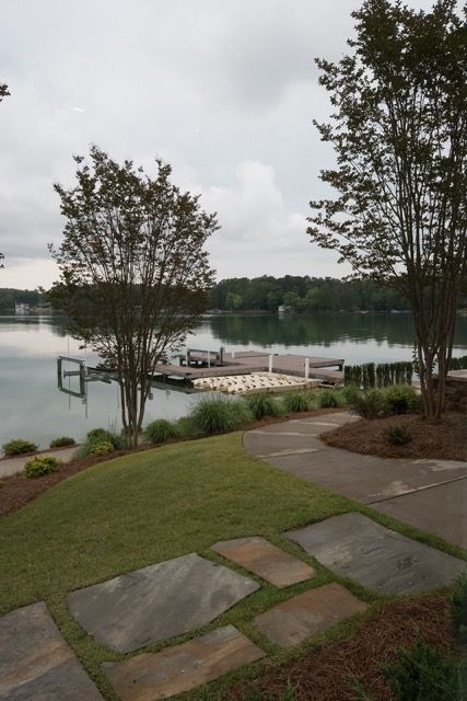 Lakefront view with a dock, trees, and a path under a cloudy sky.