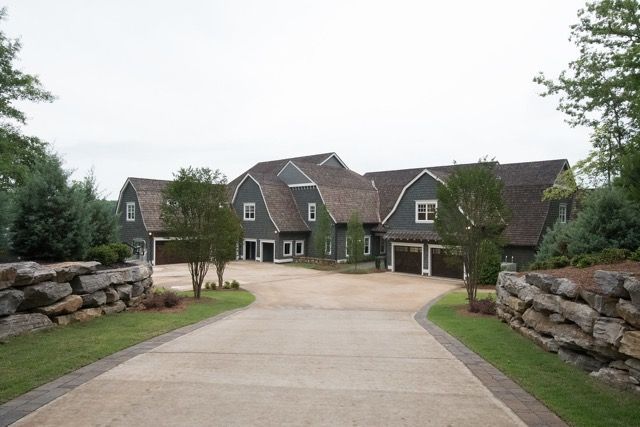 Dark gray house with brown roof, concrete driveway, and stone walls.