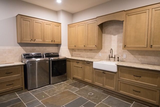 Laundry room with cabinets, stainless steel machines, sink, and stone tile floor.