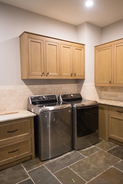 Laundry room with stainless steel washer/dryer, tan cabinets, and stone tile floor.