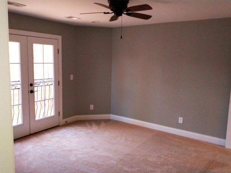 Empty bedroom with French doors to a balcony; beige carpet, gray walls, ceiling fan.