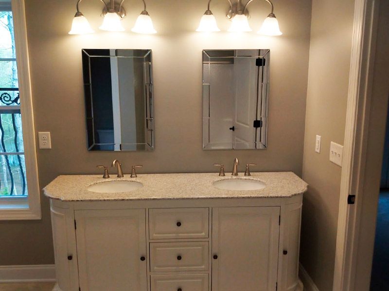 Bathroom with double sinks, white vanity, granite countertop, two framed mirrors, and sconce lighting.