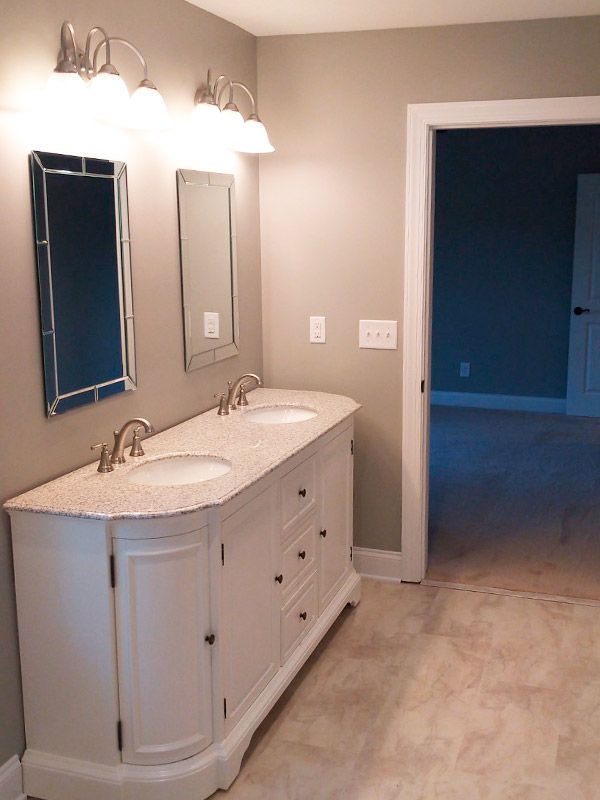 Bathroom with white vanity, dual sinks, mirrors, and a door leading to a room with blue walls.