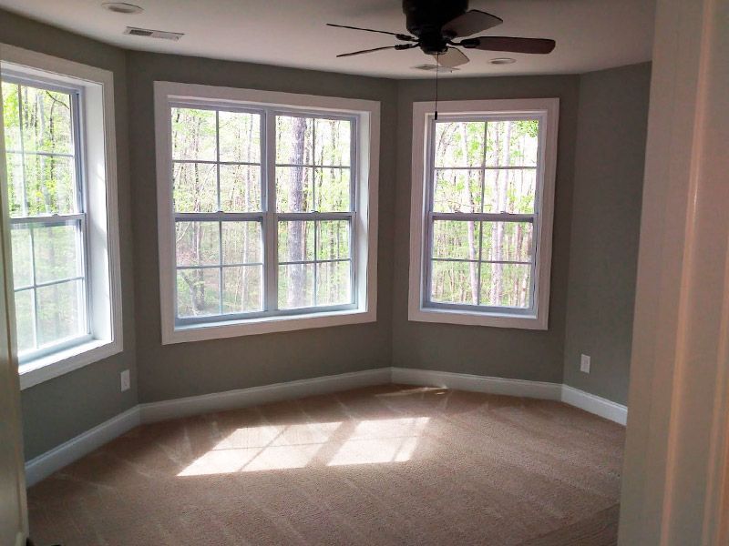 Empty room with gray walls, three windows, and brown carpet.