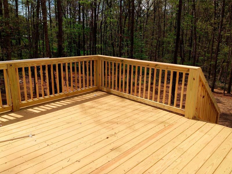 Wooden deck with railing in a wooded area, bathed in sunlight.