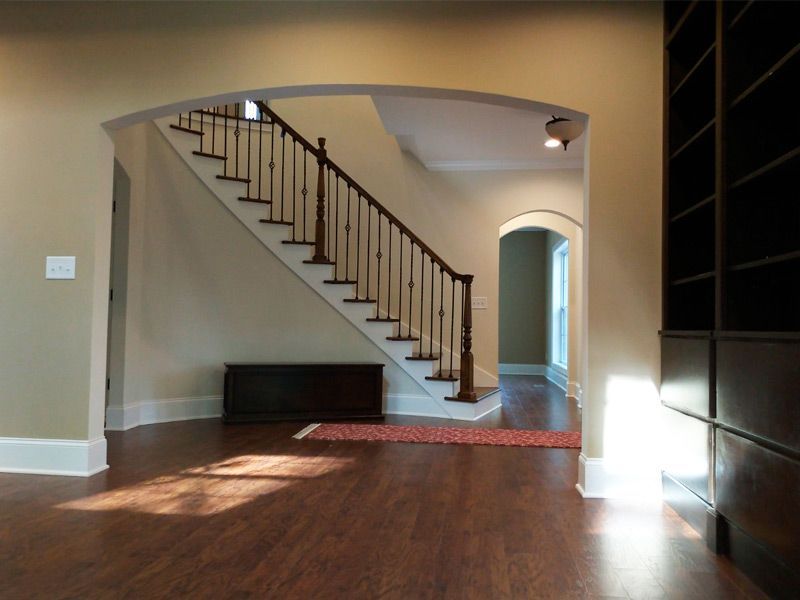 Interior view of a home with a staircase, hardwood floors, and built-in bookcase. Beige walls and natural light.