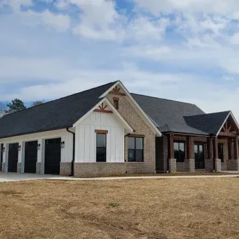 A modern, single-story house with white, gray, and brown siding and a black roof under a cloudy sky.