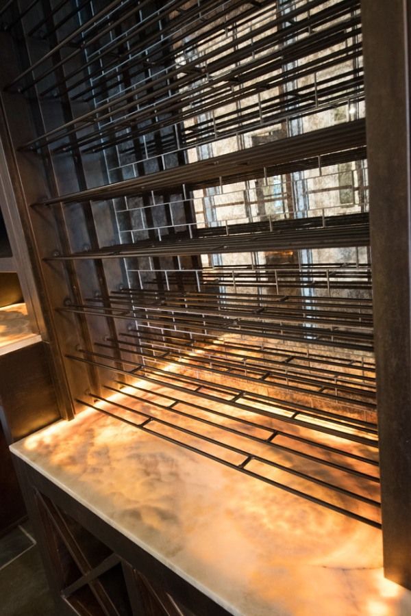 A dark metal wine rack with horizontal and vertical bars, lit from below, in a dim setting.