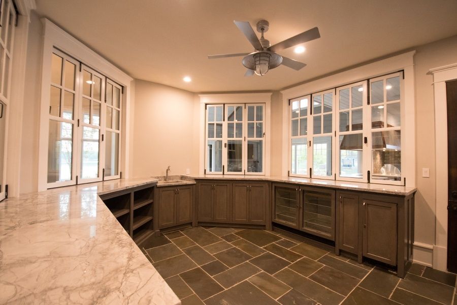 Room with marble countertop bar, slate tile floor, gray cabinets, and large windows.