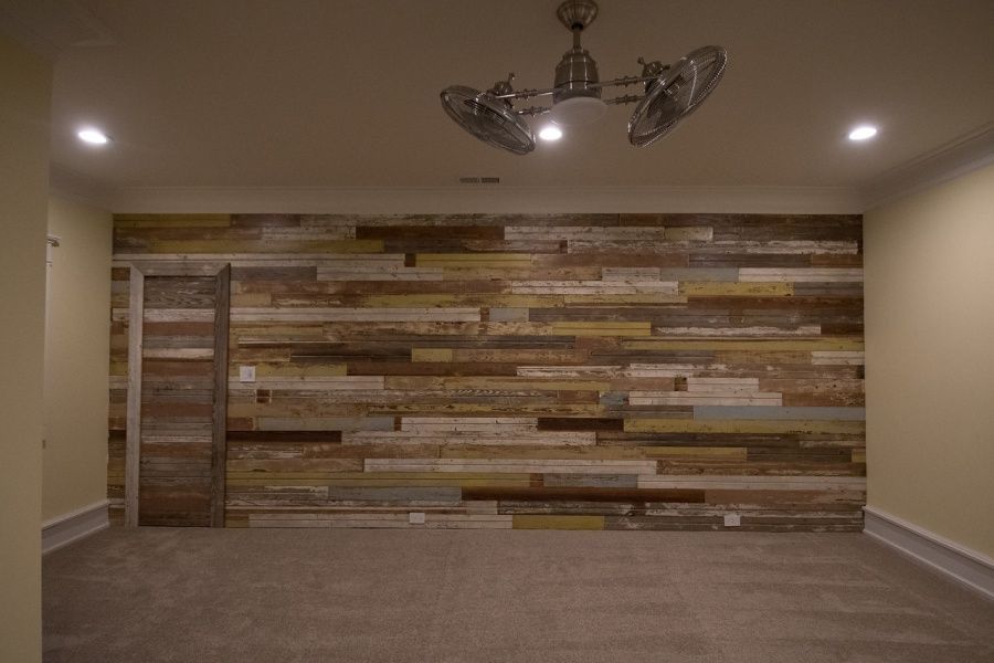 Empty room with a reclaimed wood accent wall, carpet, and ceiling fan.
