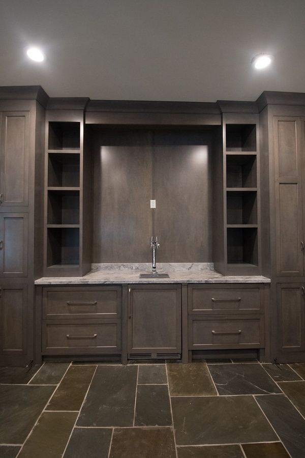 Dark wood bar area with open shelving, drawers, and sink on a slate floor.