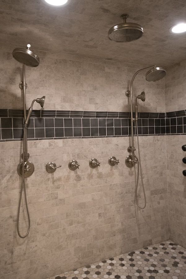 Luxurious shower with dual showerheads, multiple faucets, and gray/beige tile.
