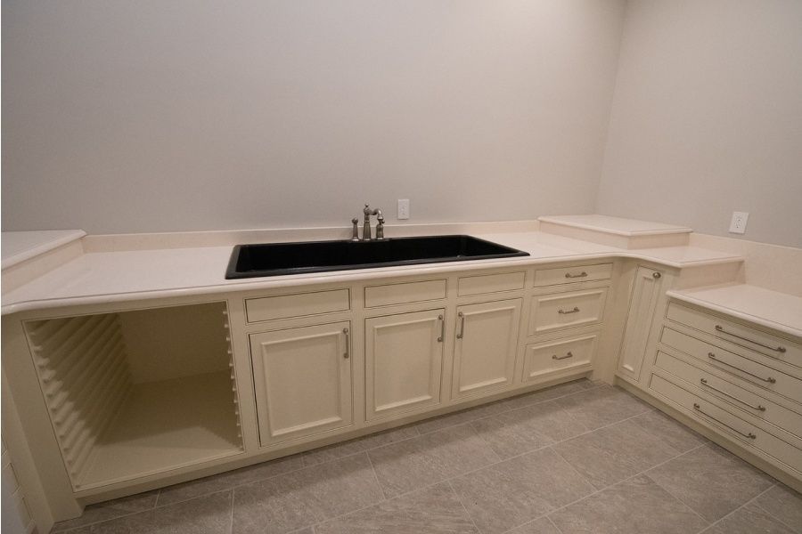 Laundry room with cream cabinets, a large black sink, and light-colored countertop.