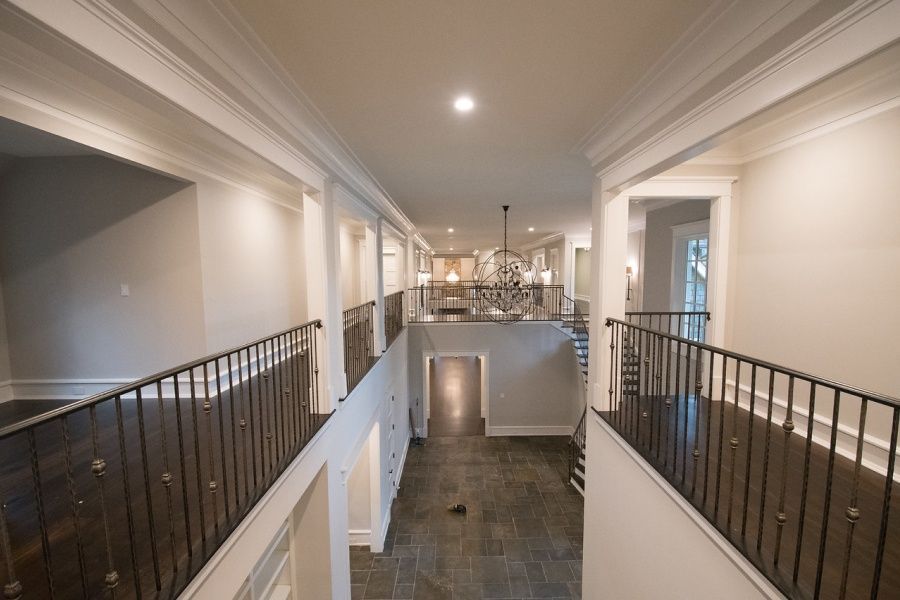 Balcony hallway with dark floors, white walls and trim, wrought iron railings, and a chandelier.