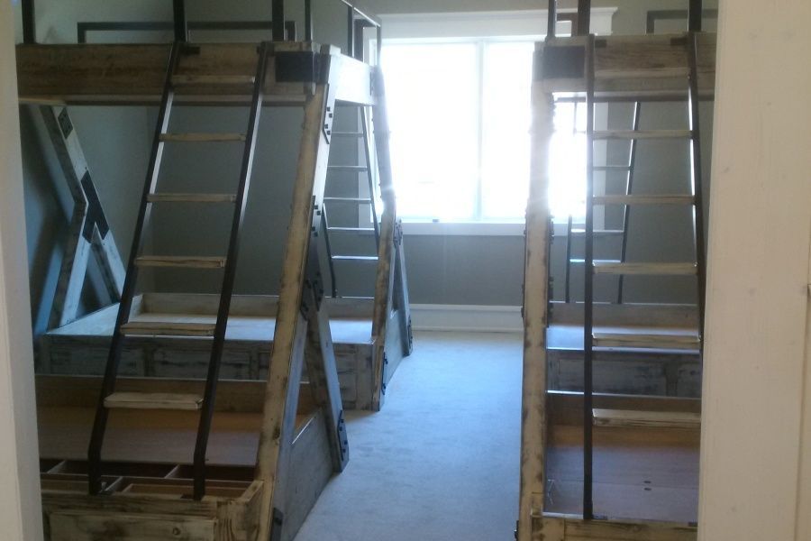 Two rustic bunk beds with ladders face a window in a room.