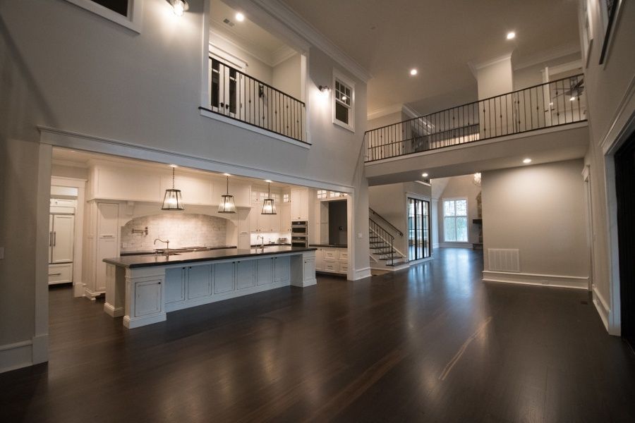 Spacious, modern home interior with dark wood floors, a kitchen, and a balcony overlooking the main living area.