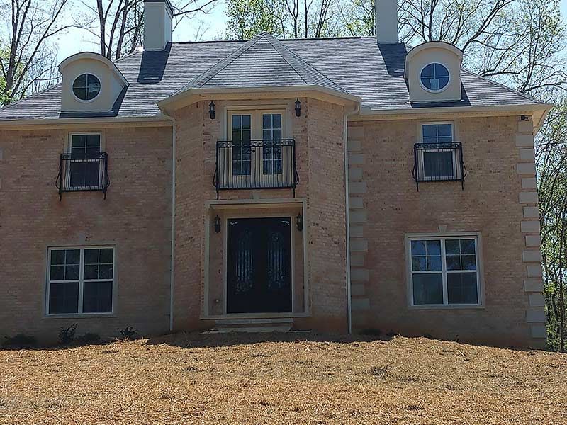 Tan brick house with black roof, ornate doorway, and two round windows.