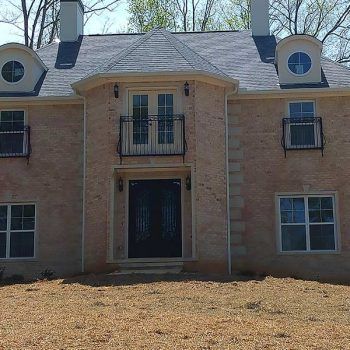 Beige brick two-story house with black doors, windows, and railings.