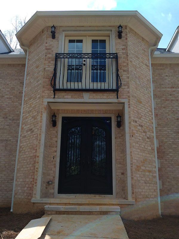 Stone brick facade with balcony, black double doors, and sconce lighting.