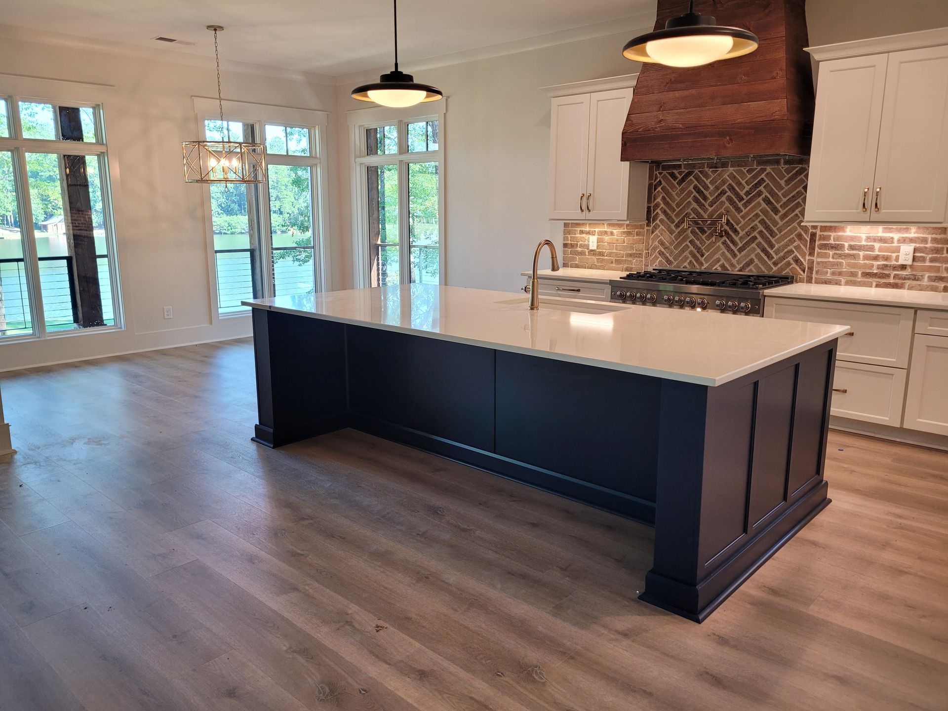 Spacious kitchen with a navy island and white countertops. White cabinets, wood hood, and large windows.