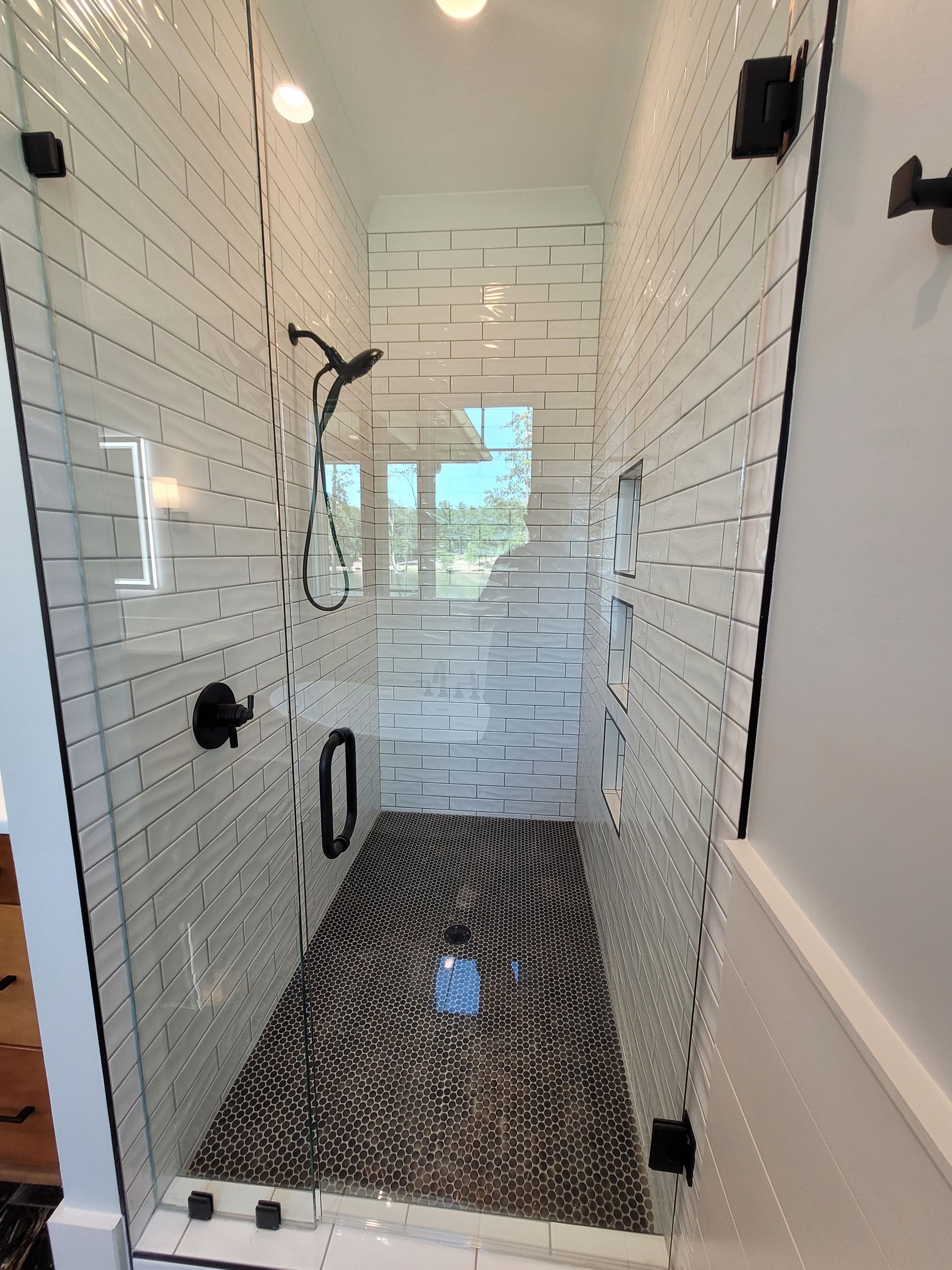 Glass-walled shower with white subway tile walls, a black and gray patterned floor, and black fixtures.