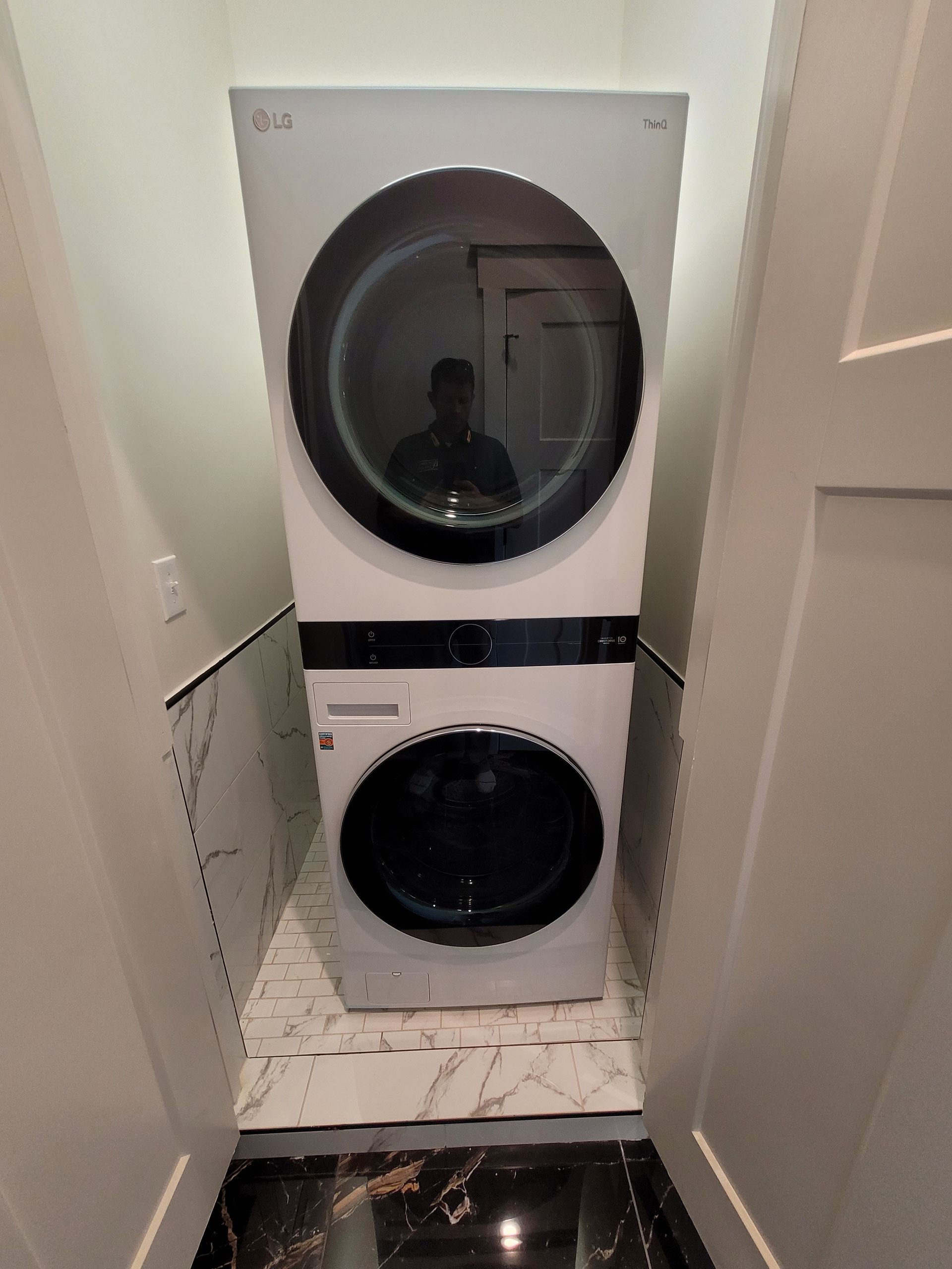 Stacked white LG washer and dryer inside a narrow laundry closet.
