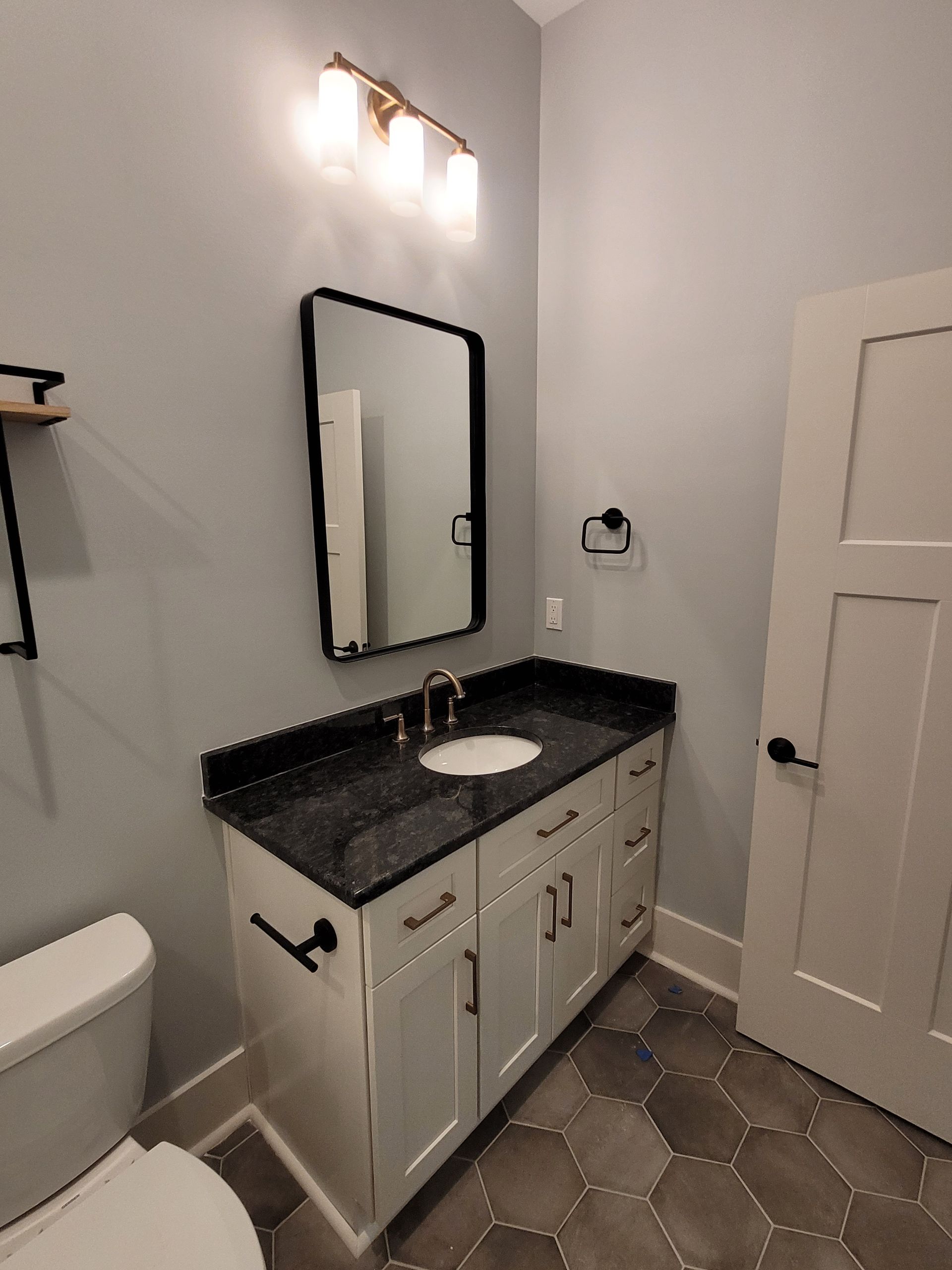 Bathroom with white vanity, black countertop, black-framed mirror, and gray walls.
