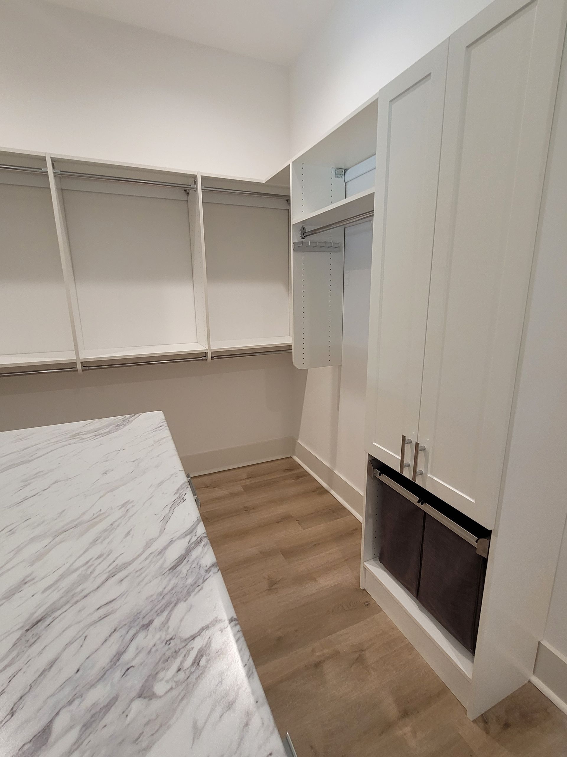 Walk-in closet with white shelves and cabinets, marble-look countertop, and wood flooring.