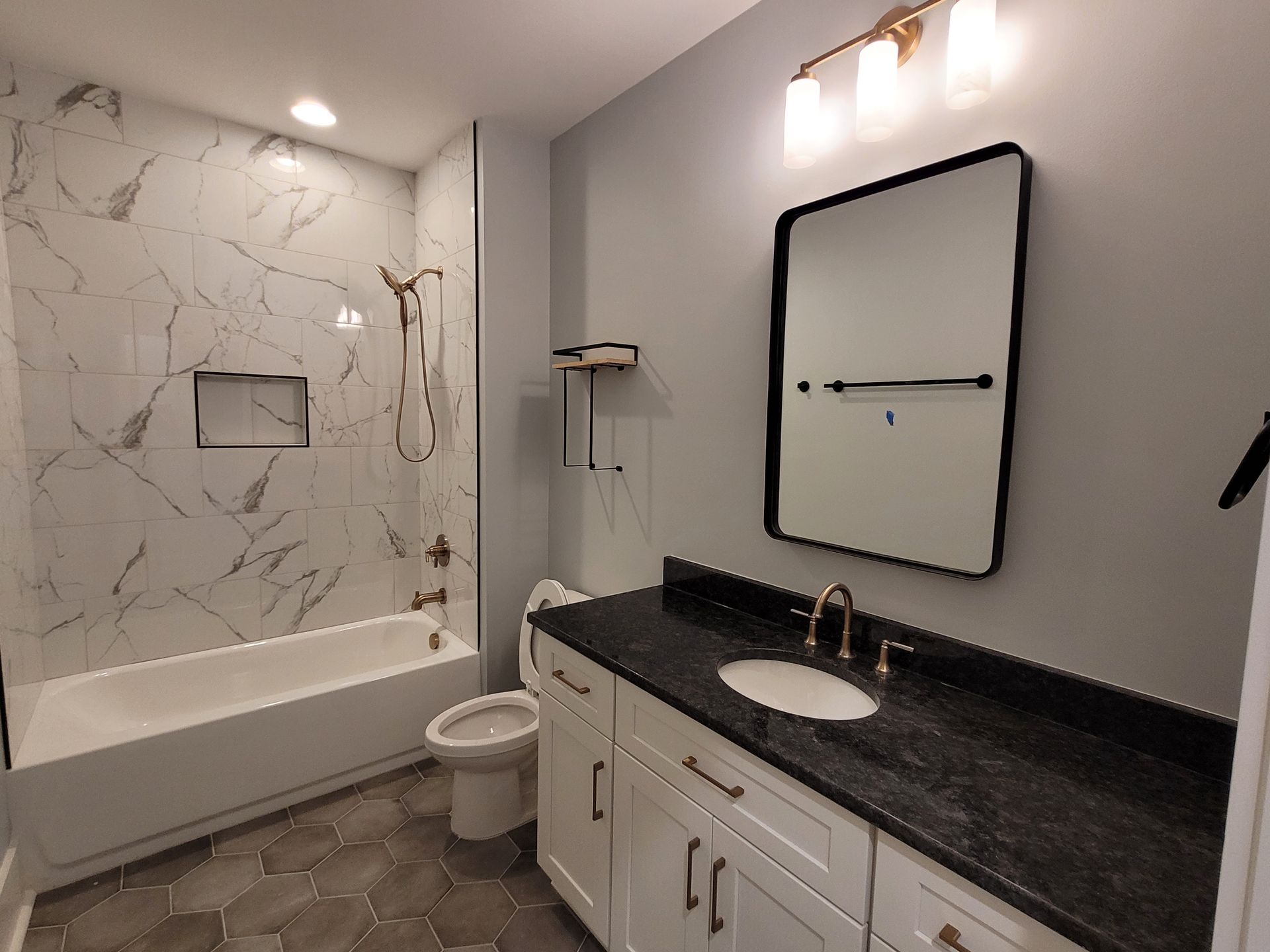 Bathroom with white marble shower, white vanity, black countertop, and hexagonal floor tiles.