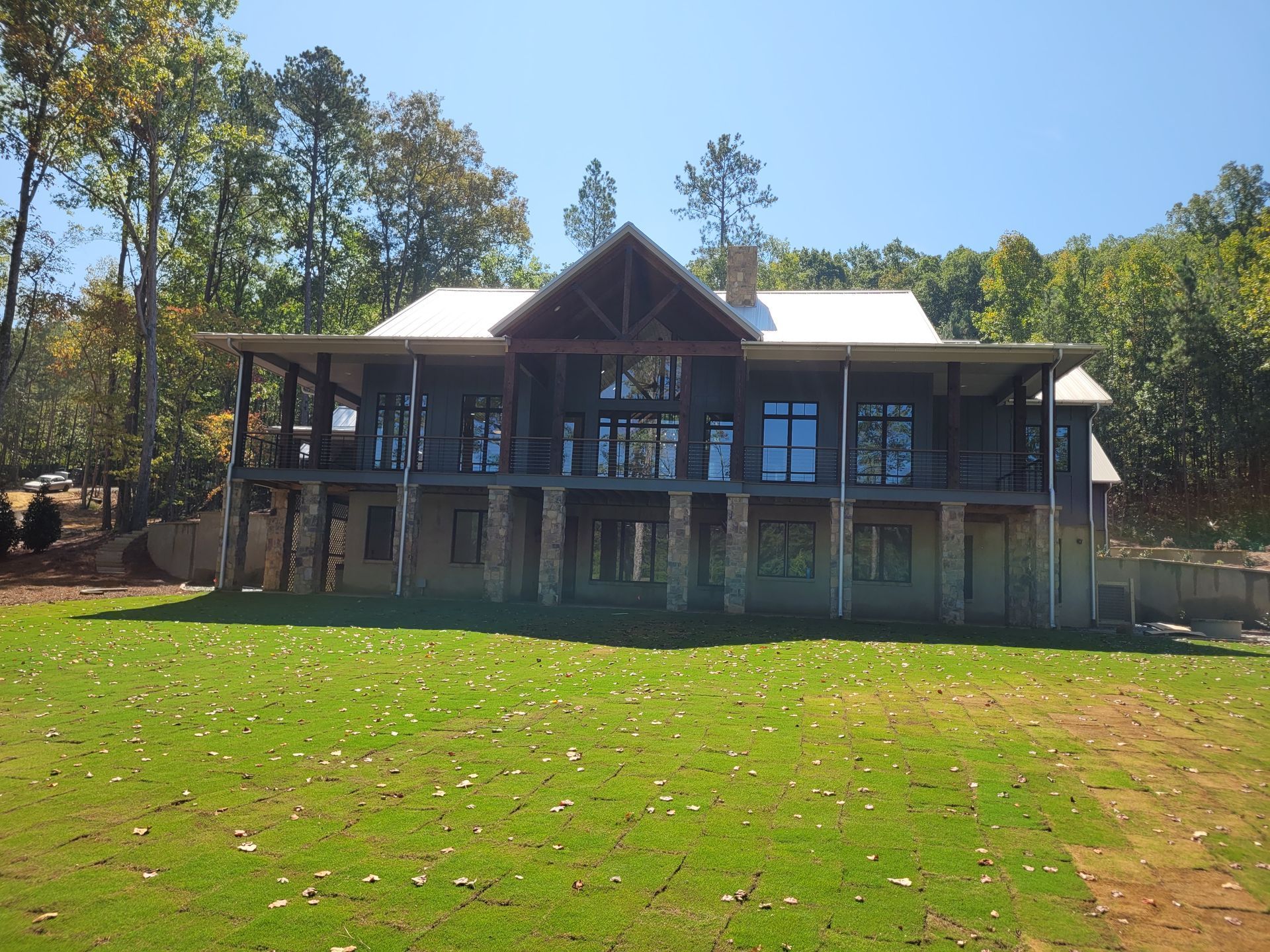 Two-story modern house with a porch and stone columns, surrounded by trees on a sunny day.