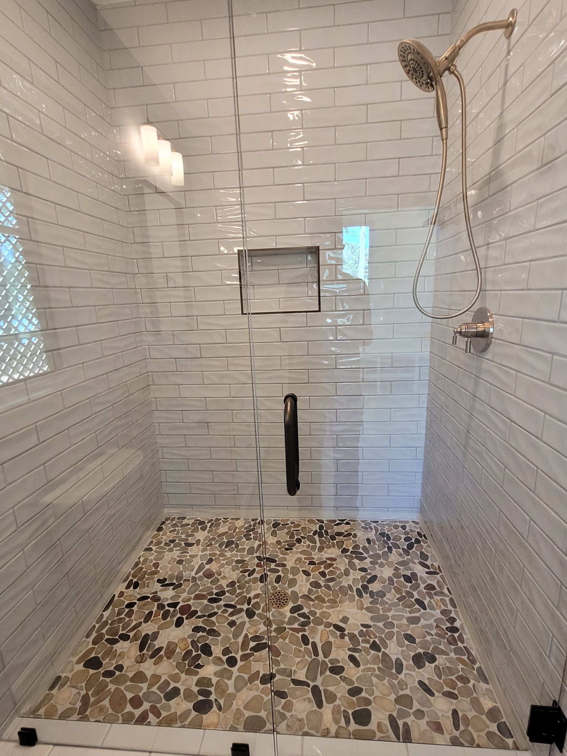 Shower with pebble floor, glass walls, white brick-style tile, and bronze fixtures.