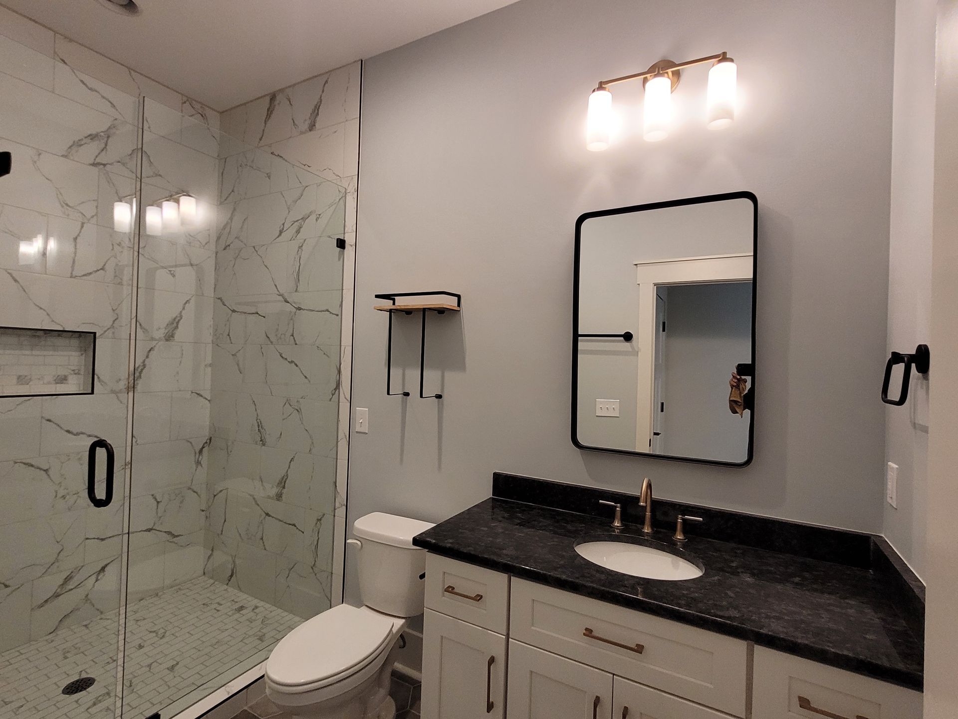 Bathroom with a white vanity, black countertop, and marble shower.