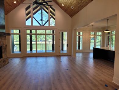 Spacious living room with large windows overlooking a lake, wood floors, and a vaulted ceiling.