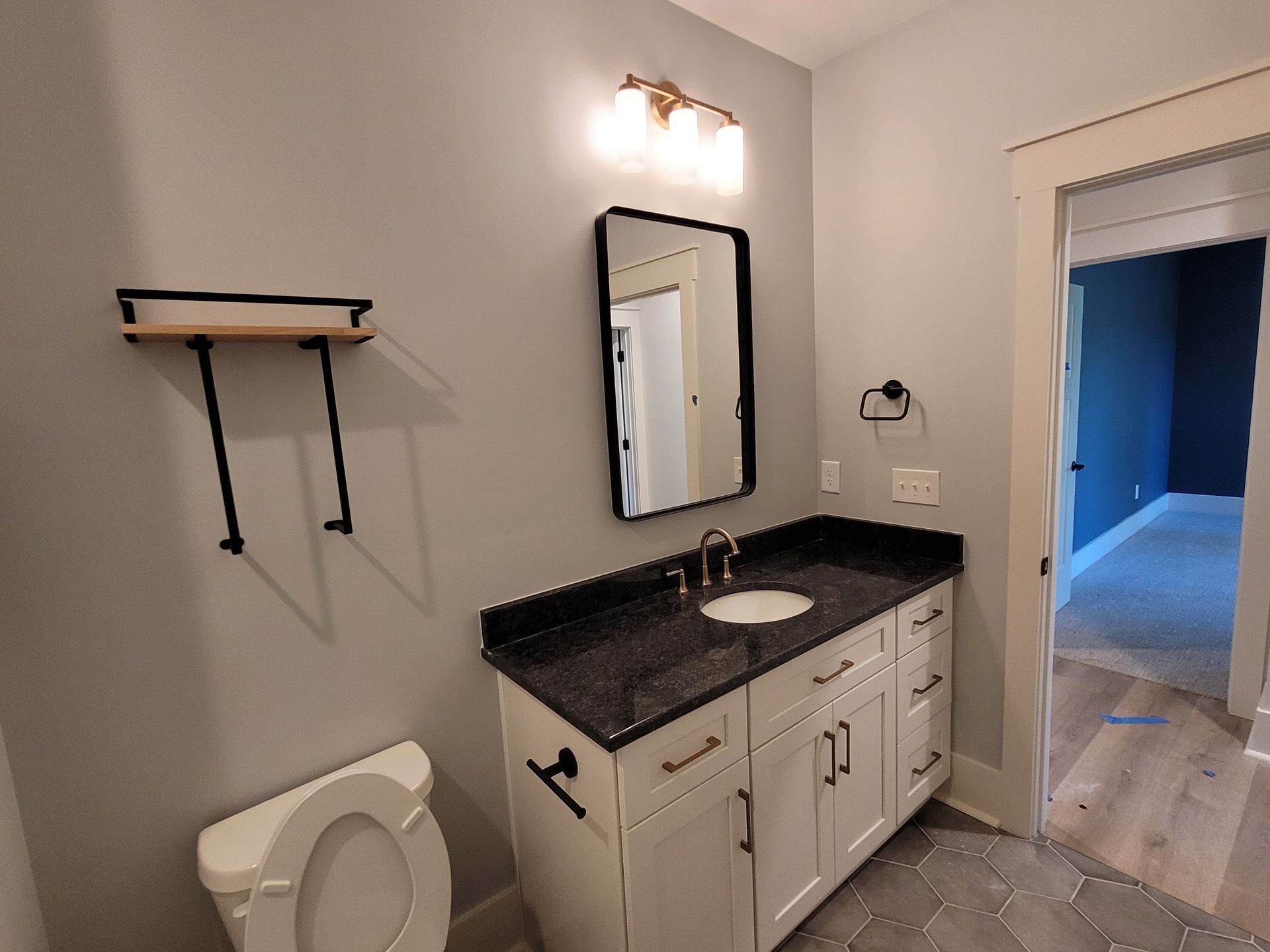 Bathroom with white vanity, black countertop, round mirror, and light fixture. Grey walls and flooring.