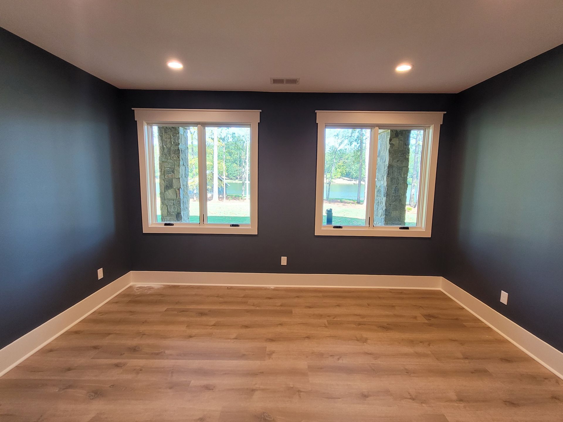 Empty room with blue walls, white trim, two windows, and wood-look flooring.