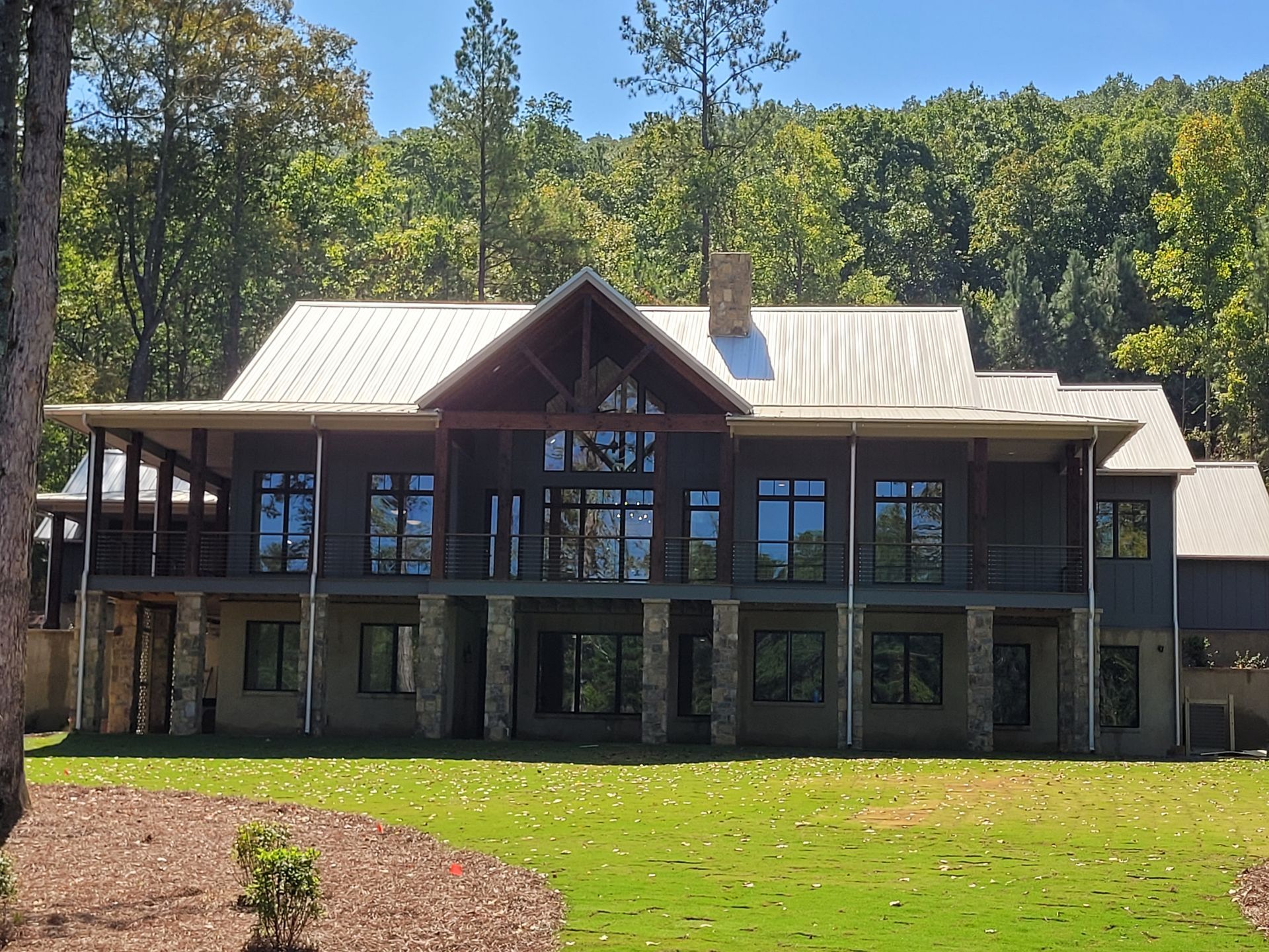 Large two-story house with a covered porch, stone columns, and large windows, set in a wooded area.