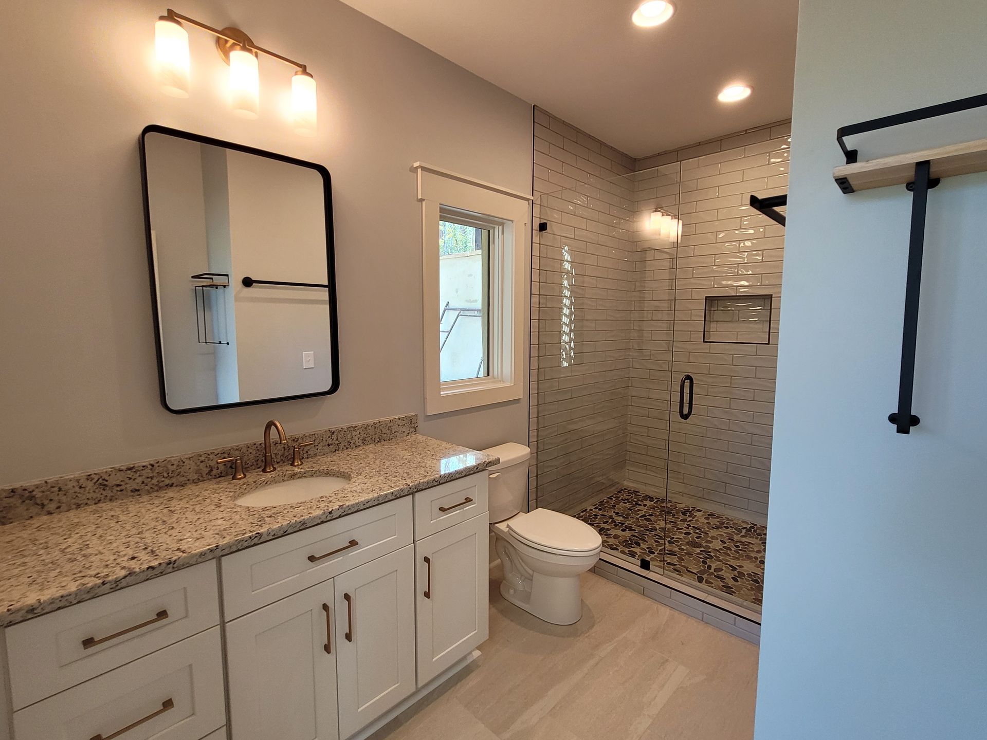 Bathroom with white cabinets, granite countertop, glass shower, and a rectangular mirror.