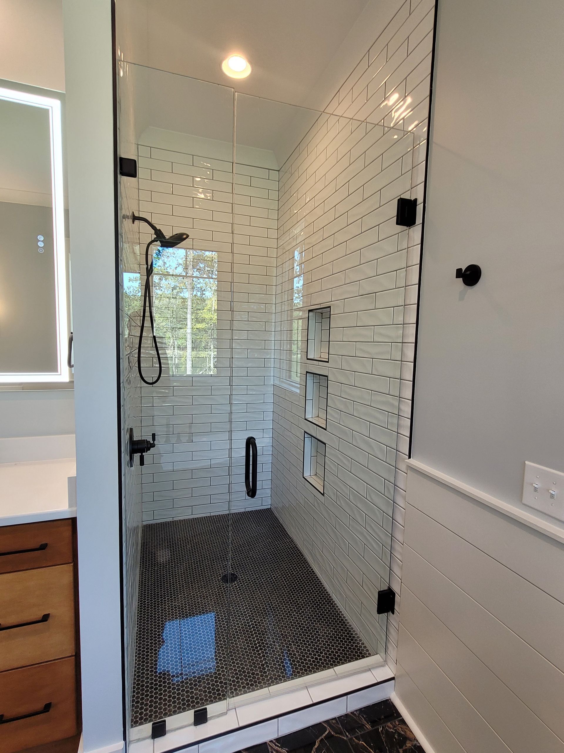 Glass shower with black and white mosaic tile, dark fixtures, and a wood vanity.