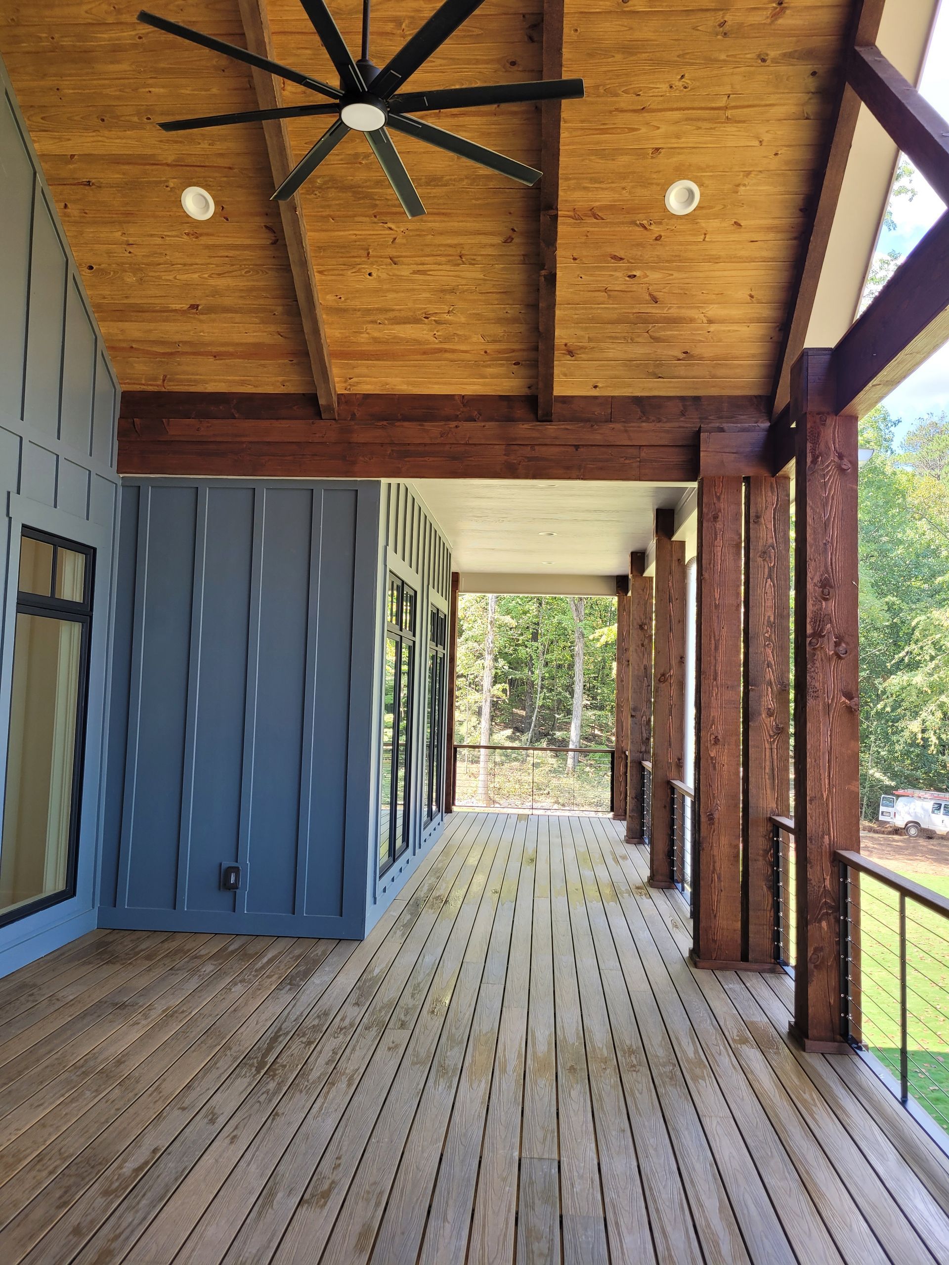 Wooden deck with a blue wall, brown support beams, and a ceiling fan.