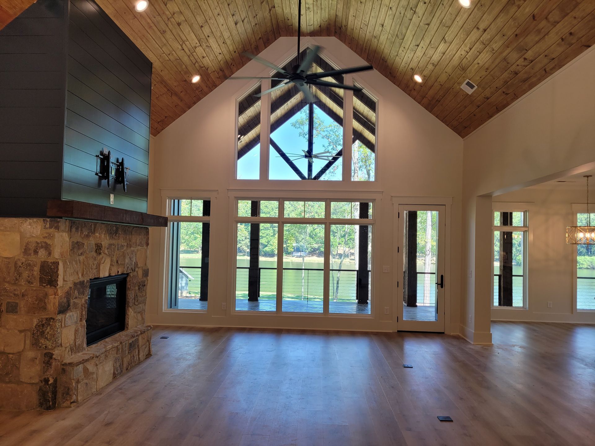 Spacious room with vaulted ceiling, large windows overlooking water, fireplace, and light wood floors.